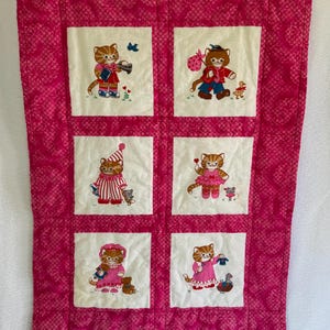 May include: A quilted wall hanging with six embroidered squares, each showcasing a different cat character in various outfits. The background is a bright pink with a textured pattern. The cats are depicted with unique accessories and poses.