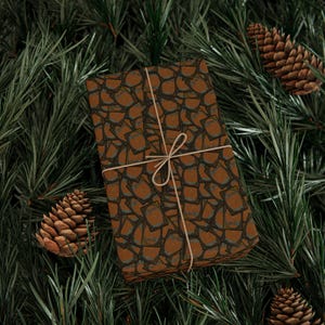 May include: A wrapped gift with brown patterned paper tied with twine, resting on a bed of green pine needles. Two pine cones are visible. The gift wrap has a repeating pattern of brown shapes with dark gray outlines.