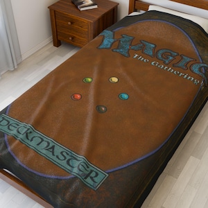 May include: A brown and black bedspread featuring the back of a Magic: The Gathering card. The design includes the text "MAGIC The Gathering" in blue and the word "DECKMASTER" in green. The bedspread has a distressed, vintage look.