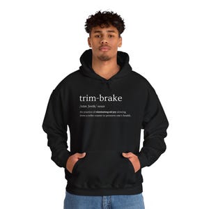 Puede incluir: Sudadera con capucha negra con el texto "trim-brake" y su definición en blanco. La definición dice: "la práctica de eliminar toda la alegría, frenando una montaña rusa para preservar la salud de uno."