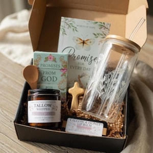 May include: A gift box filled with a glass jar with a wooden lid and straw, a small wooden cross, a jar of tallow whipped balm, a lip balm, and a book with the words "Promise for Every Day". The box contains decorative paper.