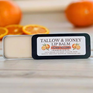 May include: A black and white label on a lip balm tin reads "Tallow & Honey Lip Balm Sweet Orange" and lists the ingredients: "100% Grass-Fed Beef Tallow, Raw Honey, Organic Beeswax, Essential Oil".
