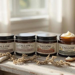 May include: Four glass jars of whipped tallow cream with black lids. The jars are labeled "Unscented", "Vanilla Bean", "Frankincense", and "Eucalyptus Lemon". A wooden spoon and lemon slice are next to the jars.