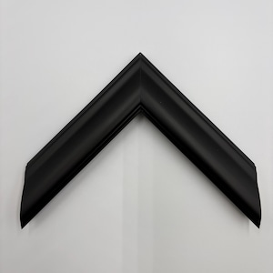 May include: A matte black picture frame corner sample featuring a clean, angled miter joint. The frame profile has a smooth, slightly curved surface with subtle ridges along the outer and inner edges, creating a simple, uniform appearance.