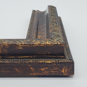 Puede incluir: Un marco de imagen marr&oacute;n oscuro con un dise&ntilde;o adornado dorado y verde. El marco tiene un acabado desgastado.