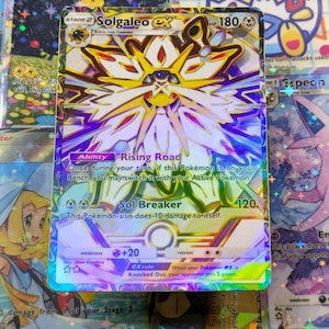 Könnte beinhalten: Eine holografische Solgaleo GX Pokémon-Sammelkarte. Die Karte zeigt eine detaillierte Illustration von Solgaleo mit einem gelben und weißen Design. Die Karte enthält Text wie "Rising Road" und "Sol Breaker".