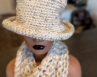 Può includere: Un cappello a cilindro all'uncinetto color crema con sottili macchie scure e una sciarpa ad anello in maglia grossa abbinata. Il cappello presenta una corona piatta e una tesa larga leggermente rialzata, con una trama aperta e testurizzata.