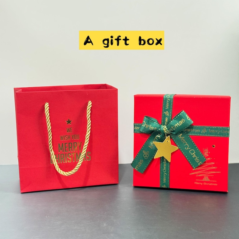 May include: Red gift box and matching gift bag. The gift box is tied with a green ribbon and gold star. The gift bag has gold rope handles and gold text that reads "We wish you Merry Christmas."