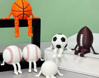 May include: A collection of sports ball figurines, including a basketball, baseballs, soccer ball, football, and golf ball. Each ball has articulated arms and legs, and is in various colors, including orange, white, black, and brown.