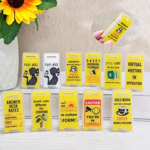 May include: A selection of yellow and white desk signs with different messages and images. Some signs read "You Are," "Arbeit Macht Frei," and "Caution You're on Camera." Other signs feature a coffee cup and the text "Coffee Brings Freedom!"