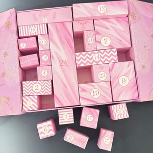 May include: A pink advent calendar with multiple numbered boxes. The boxes have various designs, including stripes, chevrons, and marble patterns. The text "Merry Christmas" is visible on the top left. The numbers 1 through 24 are visible.