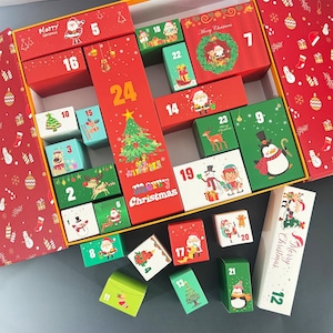 May include: A festive Christmas advent calendar with 24 numbered boxes, each with a unique holiday illustration. The boxes are red, green, and white, featuring images of Santa, reindeer, and Christmas trees. The words "Merry Christmas" are visible.