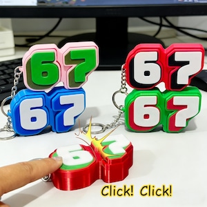 May include: Keychains featuring the number 67 in various color combinations: pink and green, blue and white, red and green. The keychains have a 3D design and are attached to a silver chain. The image also shows the text "Click! Click!"
