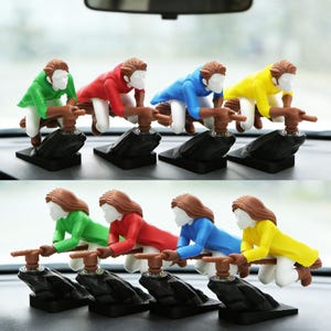 May include: A collection of eight miniature figurines depicting a person riding a broom. The figurines are in various colors, including green, red, blue, and yellow. Each figure is mounted on a black base, with brown broom handles.