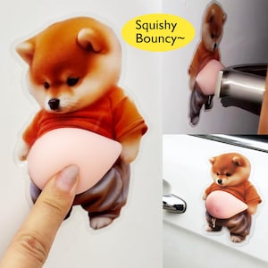 Puede incluir: Una pegatina transparente con un cachorro Shiba Inu de dibujos animados con una barriga rosada y blanda. El cachorro lleva una camisa naranja y pantalones marrones. El texto "Squishy Bouncy" está en un óvalo amarillo.