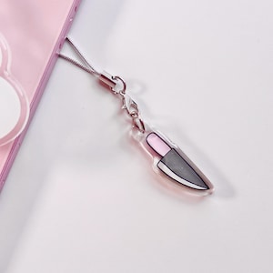 Puede incluir: Una cadena plateada con un dije de cuchillo rosa y gris. El dije de cuchillo está hecho de acrílico transparente y tiene un mango rosa y una hoja gris.