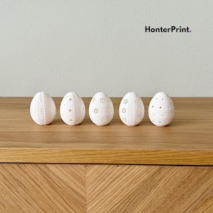 Peut inclure: Cinq œufs de Pâques décoratifs blancs avec des motifs de points et floraux complexes. Les œufs sont disposés en rangée sur une surface en bois. Le texte "HonterPrint." est visible dans le coin supérieur droit.