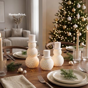 May include: Three white ceramic snowman-shaped lanterns with perforated patterns and top hats, arranged on a wooden dining table with plates, cutlery, and candles. The text HonterPrint. is visible in the upper left corner of the image.