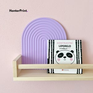 Könnte beinhalten: Ein helles Holzregal mit einer hellvioletten Wanddekoration in Bogenform und einem Kinderbuch. Das Buch hat eine Panda-Illustration und den Text "Kontrastní Leporelo se zvířátky ze ZOO". Die Wand ist hellrosa gestrichen, und der Markenname "HonterPrint" befindet sich oben links.