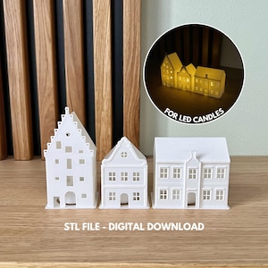 Puede incluir: Tres casas blancas impresas en 3D con detalles intrincados, diseñadas para sostener velas LED. Las casas están dispuestas en una fila sobre una superficie de madera. El texto "FOR LED CANDLES" es visible en el fondo.