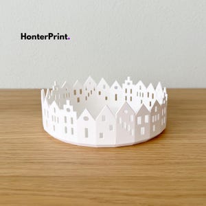May include: A white paper bowl featuring a cut-out design of houses. The bowl is on a wooden surface. The text "HonterPrint." is in the upper left corner.