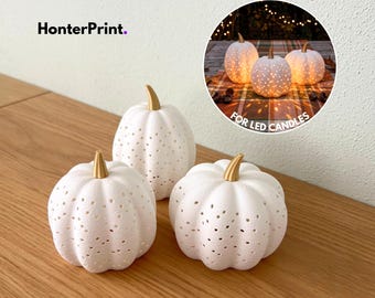 Puede incluir: Tres objetos decorativos con forma de calabaza blanca con superficies perforadas y tallos de color dorado. El texto HonterPrint es visible en la esquina superior izquierda. Un recuadro circular muestra las calabazas iluminadas desde el interior por velas LED.