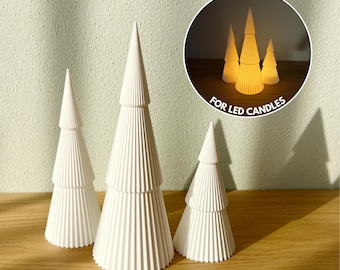 Peut inclure: Trois arbres décoratifs blancs en forme de cône à gradins avec un design nervuré. Un encart circulaire montre les arbres éclairés avec des bougies LED. Le texte "FOR LED CANDLES" est imprimé sur l'encart.