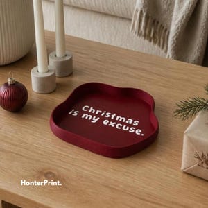 Peut inclure: Un plateau rouge foncé aux bords ondulés portant l'inscription blanche "Christmas is my excuse." Le plateau présente une finition mate lisse et un design à bassin peu profond et arrondi, offrant une surface festive pour de petits objets.