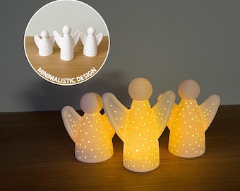 May include: Three illuminated angel figurines with a minimalist design. The white ceramic angels have outstretched wings and are dotted with small holes that emit a warm glow. The text "Minimalistic Design" is in a circle.