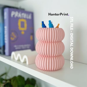 May include: A pink, 3D printed, cylindrical pen holder with a pleated design. The holder is filled with colorful pens and pencils. The image is labeled "HonterPrint. STL FILE - DIGITAL DOWNLOAD".