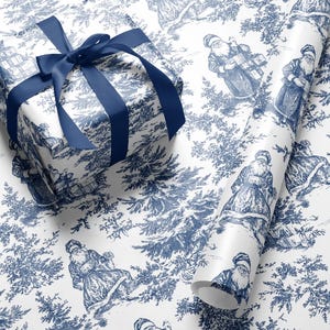Könnte beinhalten: Weißes Geschenkpapier mit blauem Toile-de-Jouy-Muster mit Weihnachtsmannfiguren und Kiefern. Ein verpacktes Geschenk mit einer blauen Satinschleife liegt neben einer Rolle passenden Papiers, ideal für Feiertagsgeschenke.