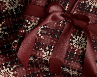 May include: A wrapped gift with burgundy plaid wrapping paper and a matching satin ribbon tied in a bow. The wrapping paper features a snowflake design in cream color. The gift is ready for a special occasion.