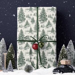 May include: A wrapped gift with a green ribbon and ornaments, featuring a cream-colored paper with a green tree pattern. The scene includes miniature snowy trees and a black toy car with a package on top, creating a festive holiday theme.