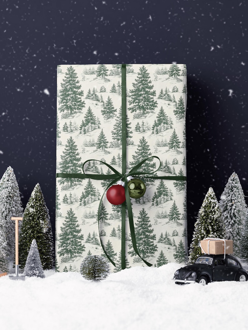 May include: A wrapped gift with a green ribbon and ornaments, featuring a cream-colored paper with a green tree pattern. The scene includes miniature snowy trees and a black toy car with a package on top, creating a festive holiday theme.