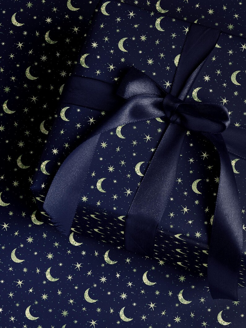 May include: A wrapped gift with navy blue paper featuring a pattern of gold crescent moons and stars. A matching navy blue satin ribbon is tied in a bow on top, creating a festive and celestial theme.