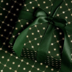 May include: A wrapped gift with dark green paper featuring a gold star pattern. A matching green satin ribbon is tied in a bow on top. The gift wrap is a festive design, suitable for holidays or special occasions.