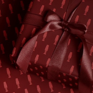 Op de afbeelding: Een ingepakte geschenkdoos met een bordeauxrood notenkrakerpatroon, vastgebonden met een bijpassend satijnen lint en strik. Het cadeaupapier en het lint zijn dieprood van kleur, wat zorgt voor een feestelijke en elegante presentatie.