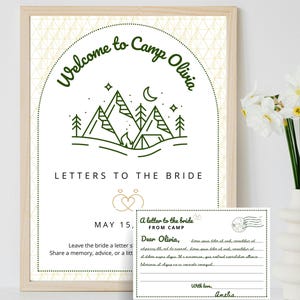 May include: A framed print with the text "Welcome to Camp Olivia" and "Letters to the Bride." A postcard with the text "A letter to the bride from Camp" is also visible. The print has a mountain and tent design.