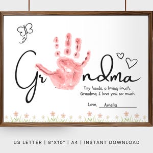 Könnte beinhalten: Gerahmter Druck mit dem Wort "Grandma" in Schreibschrift, mit einem rosa Handabdruck. Der Druck enthält den Text "Tiny hands, a loving touch, Grandma, I love you so much." und ist 20,3 cm x 25,4 cm groß.