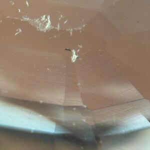 May include: Close-up of a faceted, light brown gemstone with visible inclusions and surface imperfections. The gem's cut creates multiple reflective surfaces, enhancing its clarity and brilliance. The image highlights the natural characteristics of the stone.