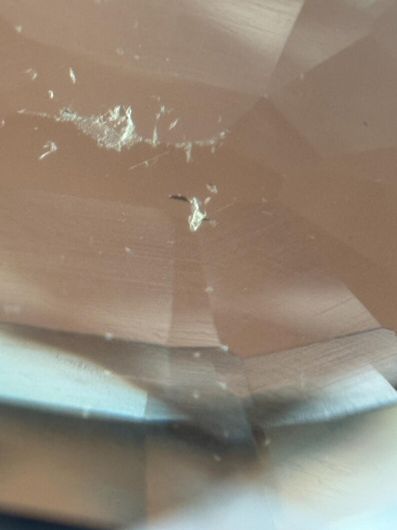 May include: Close-up of a faceted, light brown gemstone with visible inclusions and surface imperfections. The gem's cut creates multiple reflective surfaces, enhancing its clarity and brilliance. The image highlights the natural characteristics of the stone.