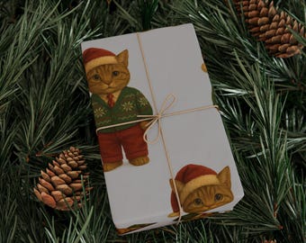May include: Wrapped gift with a light gray background, featuring a repeating pattern of a cat wearing a Santa hat, green sweater, red pants, and a tie. The gift is tied with twine and set on a bed of pine needles and pine cones.