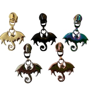 May include: Five metal zipper pulls with bat-shaped charms. The pulls are in gold, black, iridescent, bronze, and silver. Each charm has a bat silhouette with outstretched wings and a curled tail. The zipper pulls are designed for sewing projects.