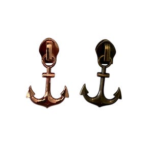 May include: Two metal zipper pulls in the shape of anchors. One is a copper color, and the other is a dark bronze color. The pulls have a loop at the top for attaching to a zipper.