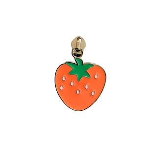 May include: A gold-coloured zip pull featuring a bright orange strawberry design. The strawberry has a green stem and small white seeds. The zip pull is attached to the top of the strawberry.