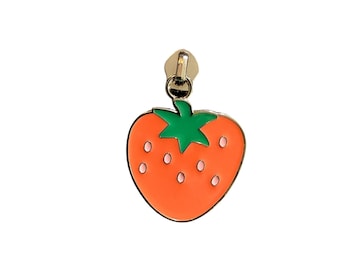 May include: A gold-colored zipper pull with a bright orange strawberry design. The strawberry has a green stem and small white seeds. The zipper pull is attached to the top of the strawberry.