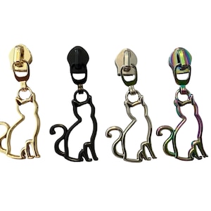May include: Four metal zipper pulls with cat silhouettes. The pulls are gold, black, silver, and iridescent. Each cat is sitting with its tail curled. The zipper pulls are attached to a metal zipper.