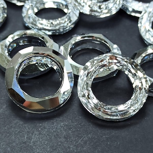 May include: Close-up of several clear, faceted crystal rings. The rings have a circular shape with a hole in the center. The facets reflect light, creating a sparkling effect. The rings are arranged on a dark surface.