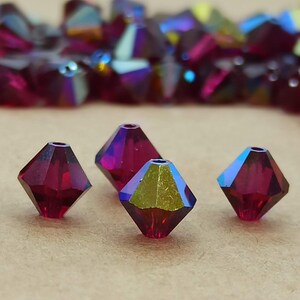 Könnte beinhalten: Vier rote, irisierende Glasperlen in Diamantform.