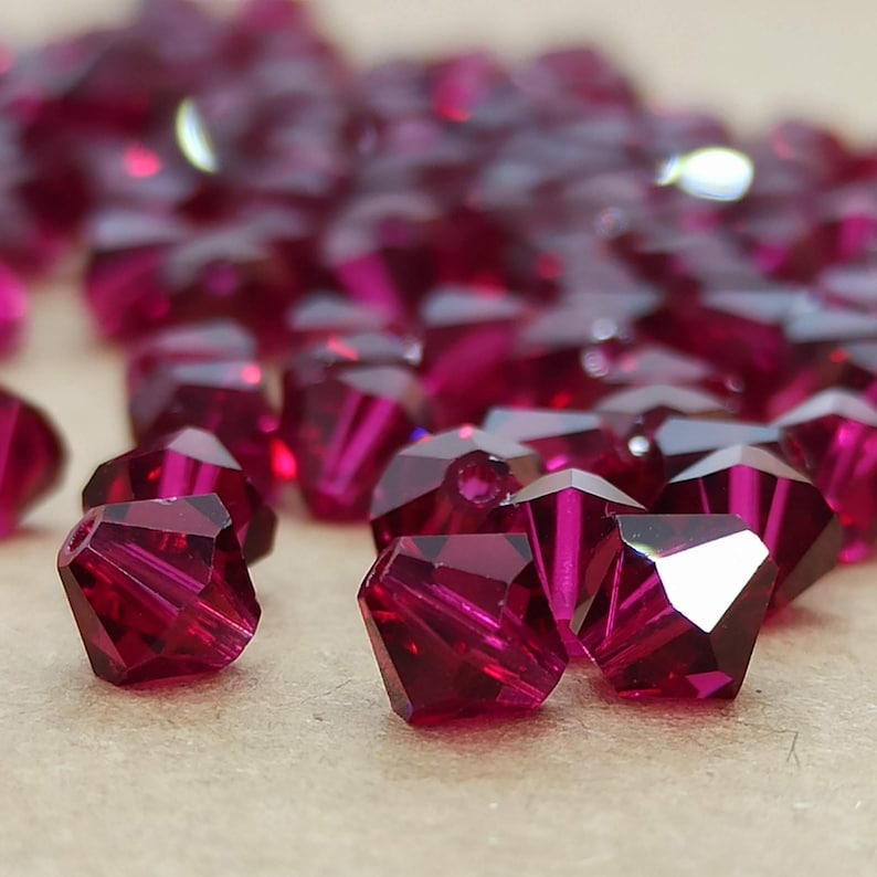 May include: A close-up of a group of small, faceted, ruby red glass beads. The beads are arranged in a random pattern on a brown surface.